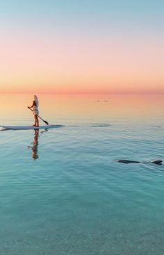 a person on a surfboard in the water at sunset or dawn with an oar