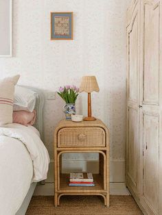 a wicker night stand with flowers on it next to a white bed in a bedroom