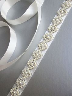 This elegant bridal belt features beautiful criss-cross pearl and crystal design. The crystal beading measures 7/8 wide and 27 long. The entire sash measures 150. Available in gold, silver or rose gold finish and with satin or organza ribbon. - The length of the beading can be Elegant Silver Bridal Belt For Bridesmaids, Elegant Crystal Bridal Belt For Formal Occasions, White Crystal Sashes For Formal Occasions, Elegant Embellished Bridal Belt For Mother Of The Bride, Elegant Bridal Belt With Sashes For Bride, Adjustable White Bridal Belt For Bridesmaid, White Crystal Sash For Formal Occasions, Elegant White Sashes With Rhinestones, Elegant Rhinestone Bridal Belt For Bridesmaids