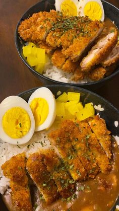 two black plates filled with rice, meat and boiled eggs on top of each other