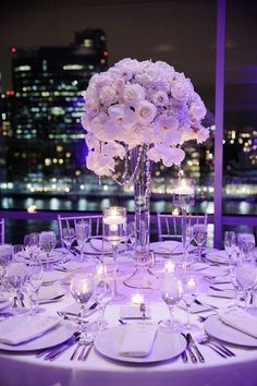 a table set with white flowers and candles for a wedding reception in front of the city skyline