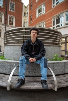 a man sitting on a bench in front of a building Streetwear Long Sleeve Track Jacket With Zip Fly, Long Sleeve Track Jacket With Zip Fly For Streetwear, Casual Track Jacket With Zip Fly For Streetwear, Relaxed Fit Half-zip Top For Streetwear, Casual Track Jacket With Embroidered Logo For Streetwear, Athleisure Sweats With Embroidered Logo For Streetwear, Streetwear Crew Neck Track Jacket With Ribbed Collar, Streetwear Half-zip Track Jacket With Ribbed Cuffs, Streetwear Track Jacket With Crew Neck And Ribbed Collar