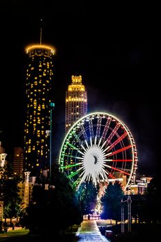 the ferris wheel is lit up at night in front of tall buildings and skyscrapers