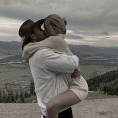 a man and woman embracing each other on top of a hill with mountains in the background