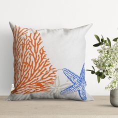 an orange and blue starfish pillow sitting on top of a table next to a vase with flowers