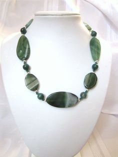 "Beautiful Green and White Striped Agate Beads in graduated ovals and rounds are combined with Swarovski Crystals in this lovely creation.  Swarovski crystal emerald green bicones accent the agates nicely.  This necklace will go with any outfit from casual to elegant.  This necklace is 18\" long with an additional 2.5\" chain extender, finished with a lobster claw clasp.  The necklace was created using: 10 mm striped round agates, 25x50mm elongated oval agates, 23x30mm flat oval agates, Swarovski emerald green 4mm bicone crystals, and 4mm fluted spacer rounds.   Agate is a variety of chalcedony with multi-colored curved or angular banding.  This is a variety of quartz. The colors are arraigned in stripes or bands.  According to Gemstone Folk lore: Agate is believed to discern truth, accept Elegant Green Gemstone Beads And Cabochons, Elegant Green Beads For Jewelry Making, Green Agate Jewelry With Faceted Beads, Elegant Green Polished Beads, Gems, And Cabochons, Green Oval Polished Beads Jewelry, Elegant Green Oval Bead Necklaces, Elegant Green Necklaces With Oval Beads, Elegant Green Oval Beads Jewelry, Green Agate Beads For Jewelry Making