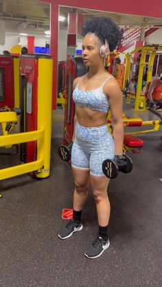 a woman standing in front of a gym machine with her hands on her hips and wearing boxing gloves