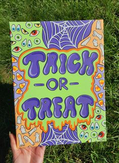 a hand holding up a trick or treat sign in the middle of some green grass