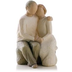 two figurines sitting next to each other on a white surface with one holding the other's head