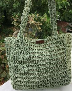 a green crocheted bag sitting on top of a white table next to trees