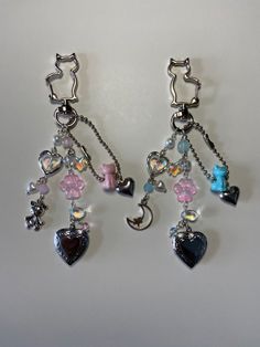 two pairs of dangling earrings with hearts and charms attached to each other on a white surface