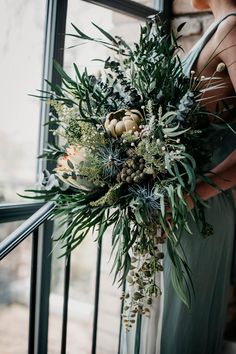 a woman in a green dress holding a bouquet of greenery and succulents