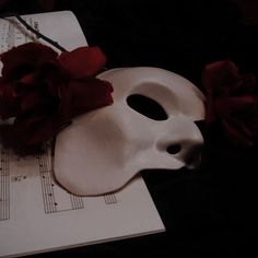 a white mask sitting on top of sheet music with red flowers in the corner next to it