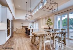 a large open concept kitchen and dining room with wood floors, white cabinets and windows