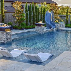 an outdoor swimming pool with lounge chairs and a slide in the back yard at sunset