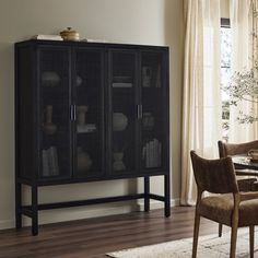 a dining room table with chairs and a bookcase in front of a large window