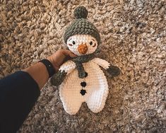 a crocheted snowman is being held by someone's hand on the carpet