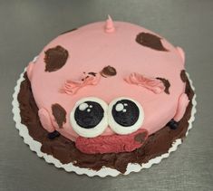 a pink cake with chocolate icing and eyes on it's face, sitting on a table