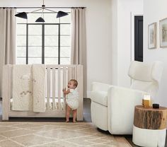 a baby standing next to a white crib in a room with furniture and decor