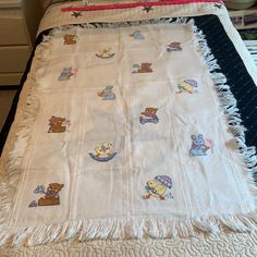 a white blanket with teddy bears on it sitting on top of a bed next to a night stand