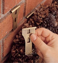 a hand holding a key to a brick wall with pine cones on the ground around it