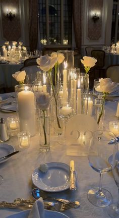 the table is set with white roses and candles for an elegant wedding reception or special event