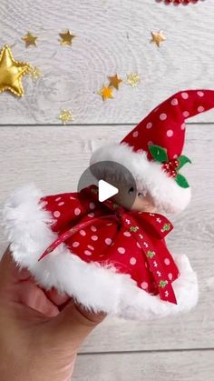 a hand holding a red and white stuffed animal with a santa hat on it's head