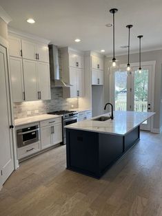 a large kitchen with an island in the middle and white cabinets on both sides, surrounded by wood flooring