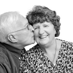 an older couple kissing each other while posing for a black and white photo in front of a white background