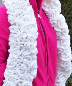 a woman wearing a pink jacket and white knitted scarf over her face with a cell phone in her hand