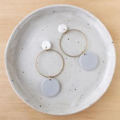 two white and gold hoop earrings sitting on top of a white plate next to a wooden table