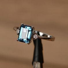 It is London blue topaz ring, the emerald cut topaz is crafted in sterling silver with white gold plated. The side stone is cubic zirconia. It is made Emerald-cut Topaz Ring In 14k White Gold, Emerald Cut Topaz Ring In 14k White Gold, Modern Emerald Cut Topaz Ring, Silver Octagon Blue Topaz Ring, Silver Emerald-cut Blue Topaz Ring, Modern Blue Topaz Jewelry Emerald Cut, Silver Blue Topaz Ring With Emerald Cut, Modern Blue Topaz Emerald Cut Jewelry, Modern Jewelry With Emerald Cut Blue Topaz