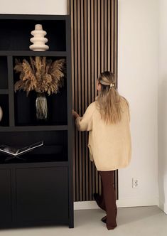 a woman standing in front of a book shelf with vases and books on it