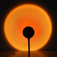 a round object with a black pole in front of it and an orange light behind it