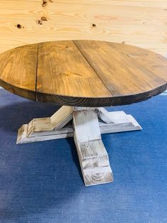 a round wooden table sitting on top of a blue carpeted floor next to wood planks