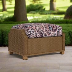 a brown wicker bench sitting on top of a stone floor next to a lush green park