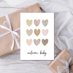 a card that says welcome baby with hearts in gold and pink on it next to two wrapped presents