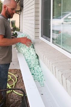 a man is working on the side of a house with green rocks in front of him