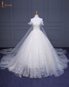 a white wedding dress on display in front of a gray wall and blue carpeted floor