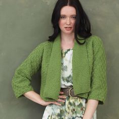 a woman standing in front of a wall with her hands on her hips wearing a green cardigan