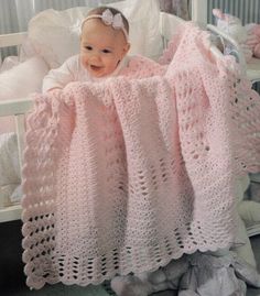 a baby in a crocheted pink blanket next to stuffed animals