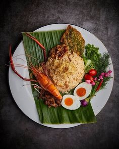 a white plate topped with meat and veggies next to eggs on top of a banana leaf