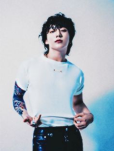 a man with tattoos standing in front of a white wall holding his hands on his hips