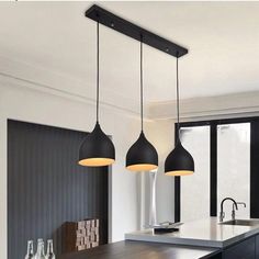 three lights hanging over a kitchen island in a room with black cabinets and white walls