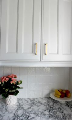 a white kitchen with marble counter tops and gold pulls on the cabinet doors over the sink