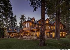 a large house with lots of windows and lights on it's front porch, surrounded by trees