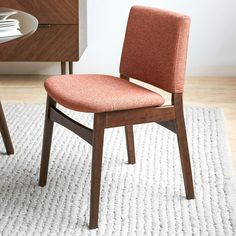 an orange chair sitting on top of a white rug in front of a wooden table