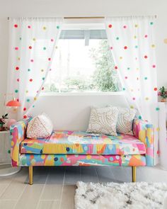 a brightly colored couch in front of a window with polka dots on the drapes