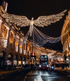 an angel statue is lit up in the middle of a busy city street at night