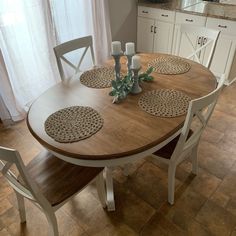 a wooden table with white chairs and placemats on it in front of a window